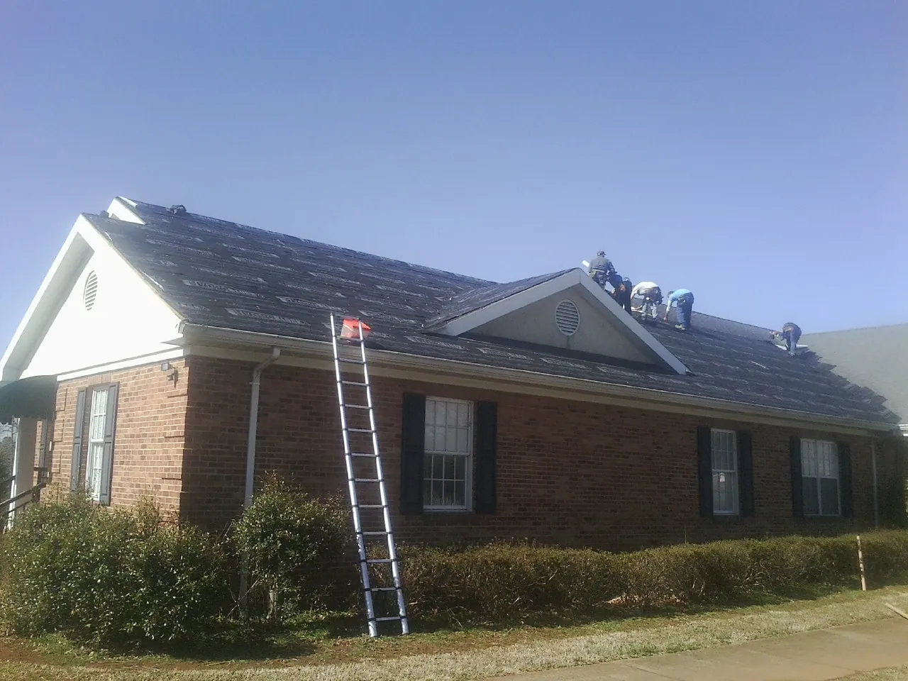 Crew tearing shingles off a brick ranch roof with a ladder set — Emergency Roof Repair work by our crew in King Ferry