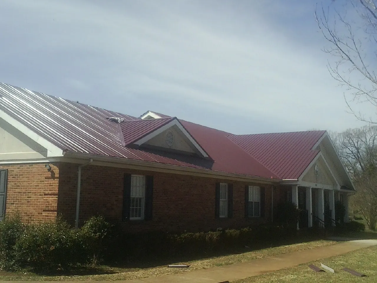 Red metal roof with gabled entries on a long brick building, from a Hail Damage Roof Repair job in King Ferry