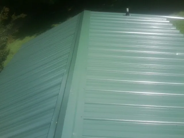 New green metal panels meeting at the ridge of a roof — Flat Roof Repair work by our crew in King Ferry