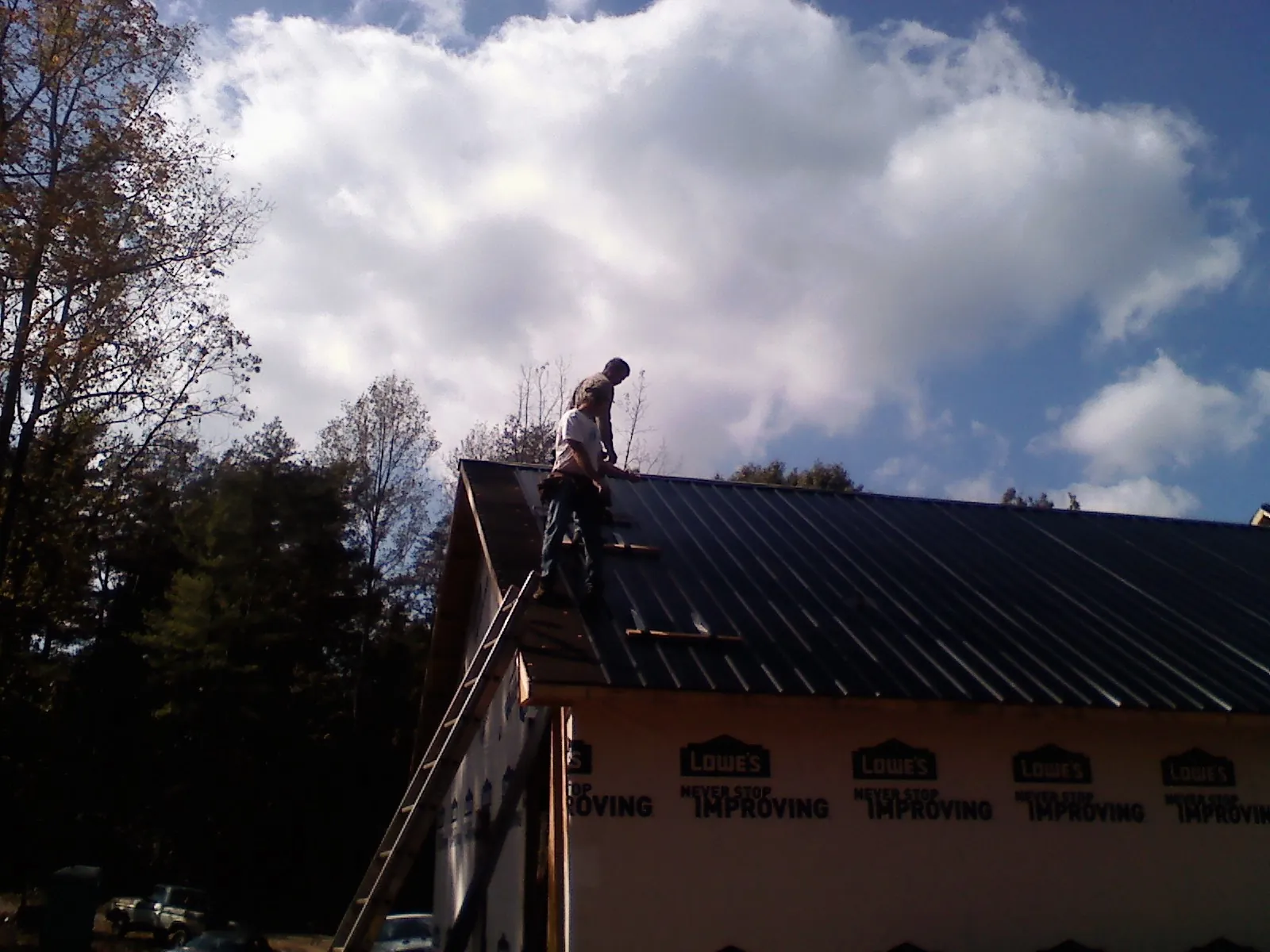 Roofer fastening dark metal panels high against a cloudy sky, from a Roof Inspection job in King Ferry