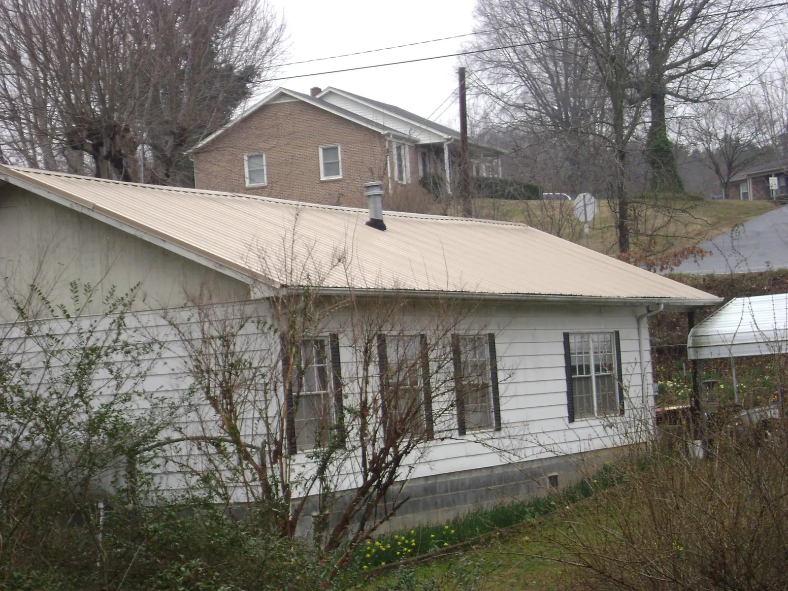 Tan metal roof on a white sided house set into a hillside — Commercial Roofing by Roofing Brothers in King Ferry